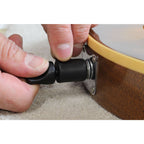Close-up of a person's hands adjusting a black cylindrical clamp or strap component attached to a brown wooden object with a beige rim.