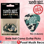 Ernie Ball camo guitar picks shown both in retail packaging and as a single pick. The product features a green, beige, and black camouflage pattern with 'Ernie Ball' printed in white.