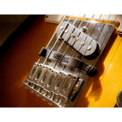 Close-up of a tremolo bridge on an electric guitar, showing the black tremolo bar, silver metal hardware, and part of the sunburst orange guitar body.