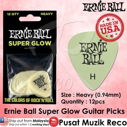 Ernie Ball Super Glow Heavy guitar picks in a 12-pack, shown in their black retail packaging alongside a single pale green pick displaying the Ernie Ball logo. The image features a pink background with text detailing the product's size, quantity, and origin.