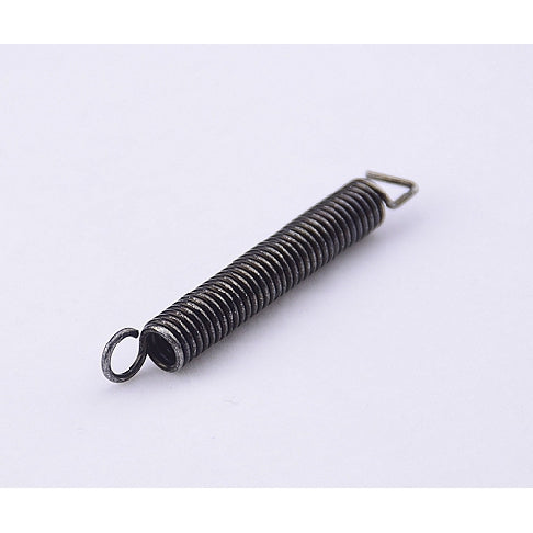 A small metal coil spring with a looped end and a small triangular tab, shown on a plain light background.