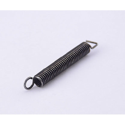 A small metal coil spring with a looped end and a small triangular tab, shown on a plain light background.