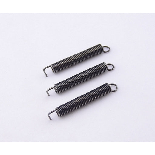 Three small dark metal compression springs with looped ends, arranged diagonally on a plain white background.