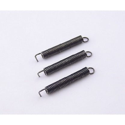 Three small dark metal compression springs with looped ends, arranged diagonally on a plain white background.