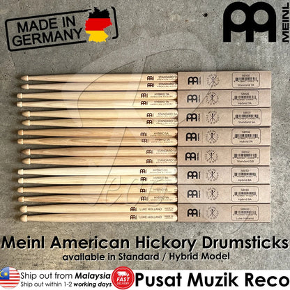 A set of Meinl American Hickory drumsticks arranged horizontally, with their original cardboard boxes stacked on top. The background is a textured gray concrete surface.