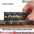 A hand holding a black RM Guitar Tools String Action Ruler with white text, against the background of a guitar fretboard.